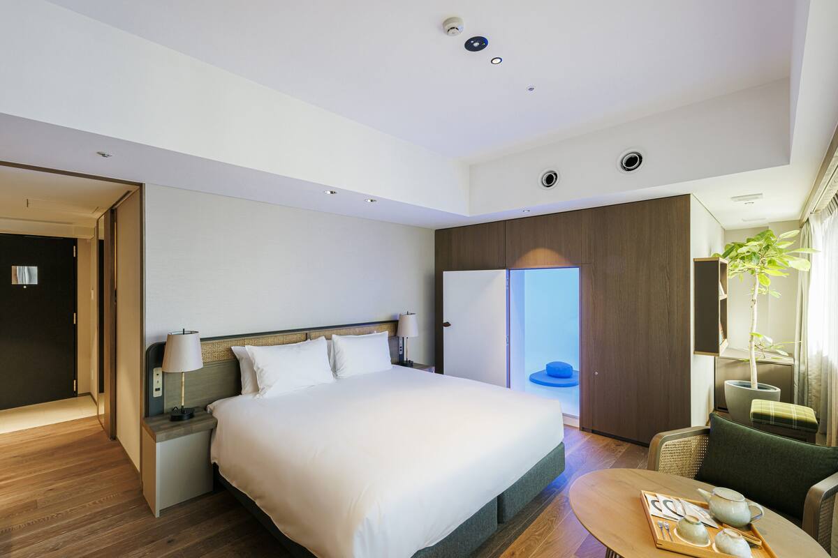 Ein modernes Hotelzimmer mit einem großen Bett, Nachttischen, einer Sitzecke mit einem Tisch und einem Kleiderschrank.