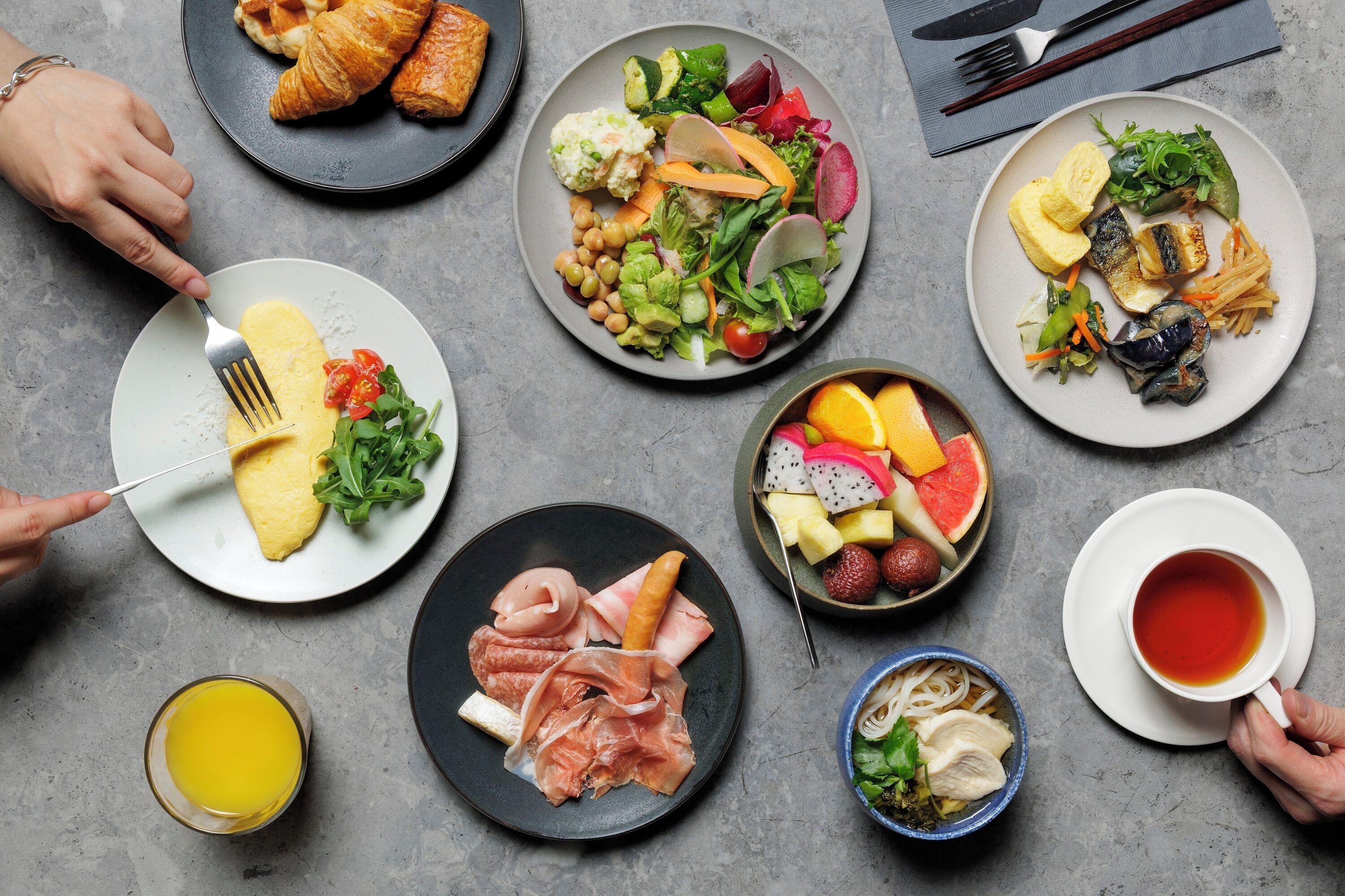 Uma mesa com diversos alimentos, incluindo ovos, salada, frutas e uma xícara de chá.