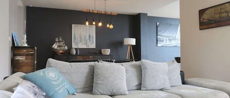 A modern living room with a sectional sofa, a dark accent wall, and a ship-themed artwork.