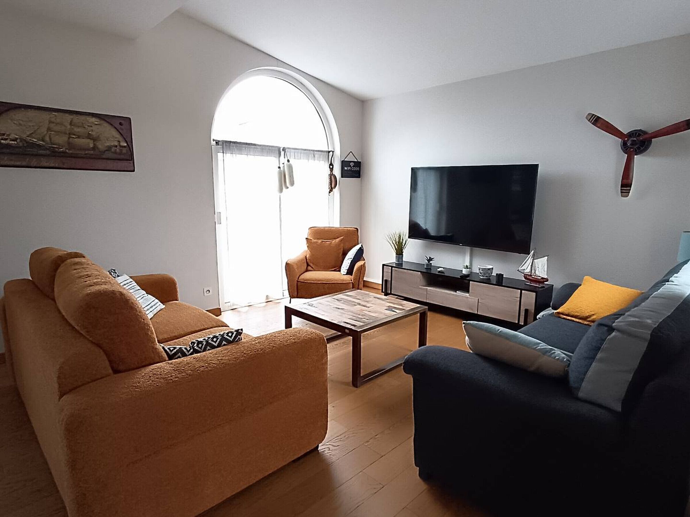 A living room with a sofa, armchair, coffee table, TV, and a ceiling fan.