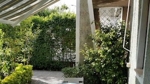 Un patio al aire libre con una mesa cubierta por un mantel floral, rodeado de sillas blancas.