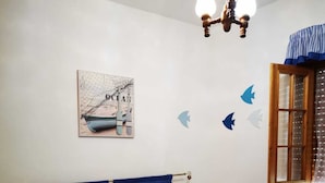 Un dormitorio con cama, mesita de noche, estante en la pared, ventana con cortinas y decoración en la pared.