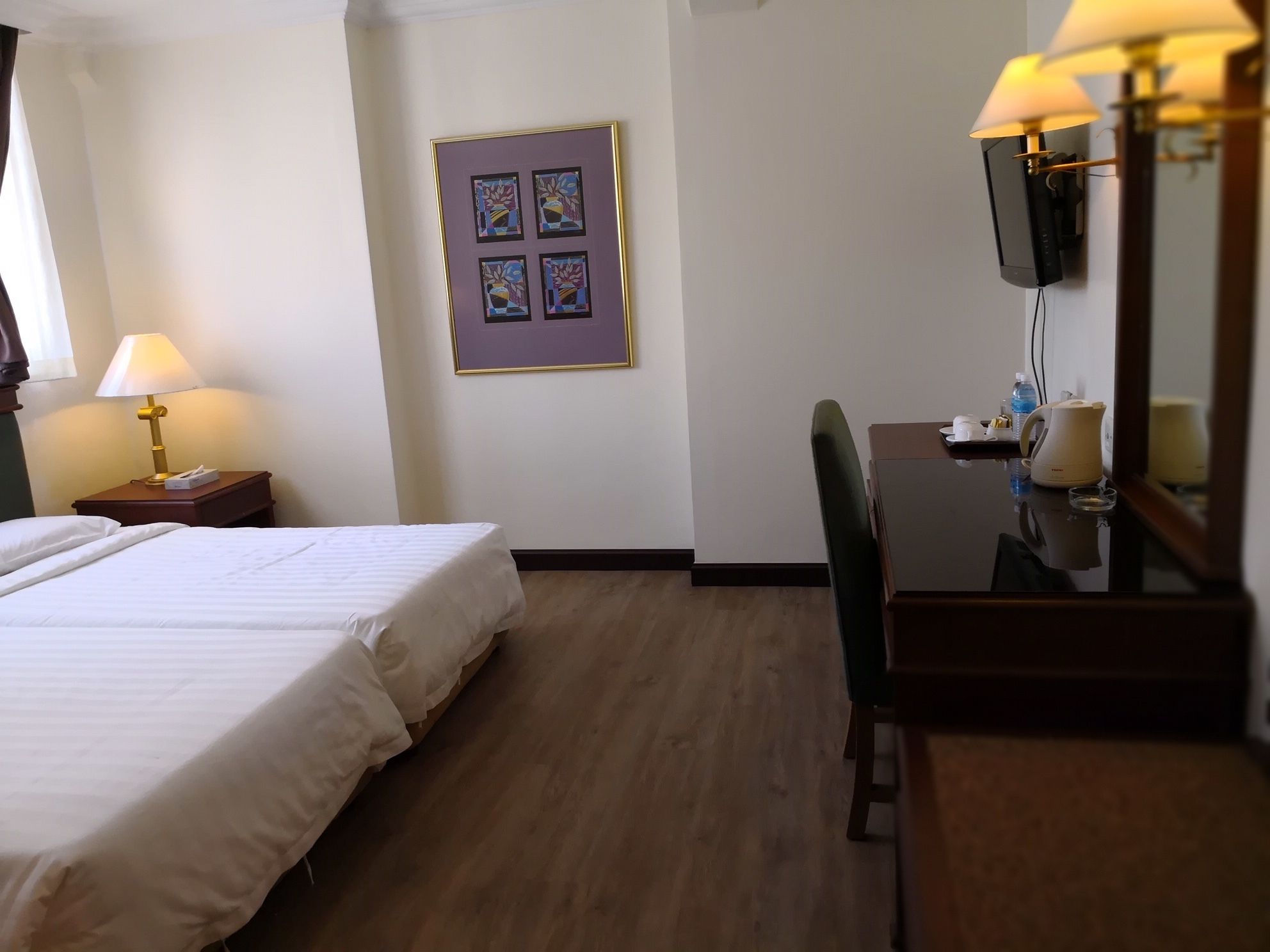 A hotel room with two beds, a desk with a chair, a television, and a framed artwork on the wall.