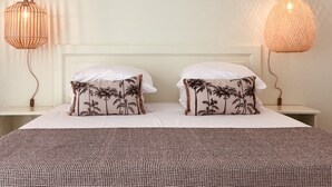 A bed with two white pillows, a patterned bedspread, and two wall-mounted lamps with a woven design. - Hotel Pelican (Schoelcher)
