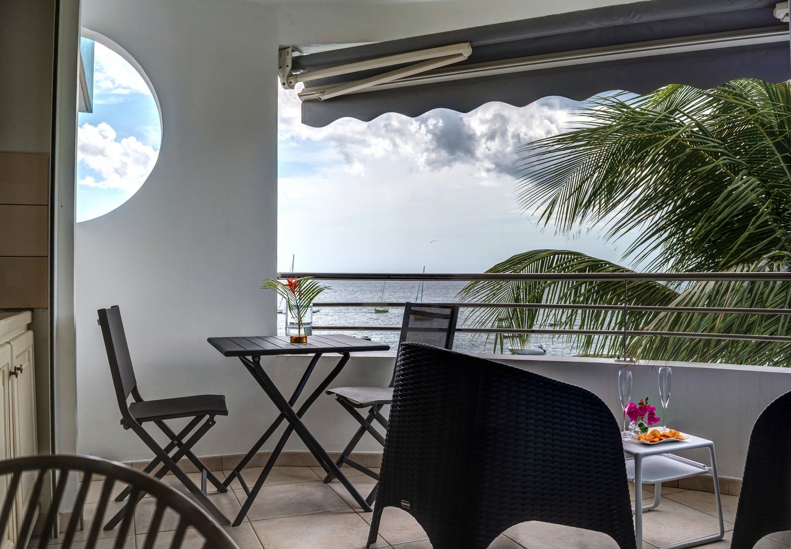 Un balcón con vista al mar, una mesa con sillas y una planta en maceta.