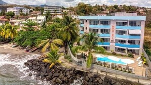 A hotel with a pool, surrounded by palm trees and a rocky shoreline. - Hotel Pelican (Schoelcher)