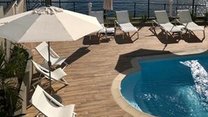 A poolside area with lounge chairs and umbrellas, overlooking a body of water. - Hotel Pelican (Schoelcher)