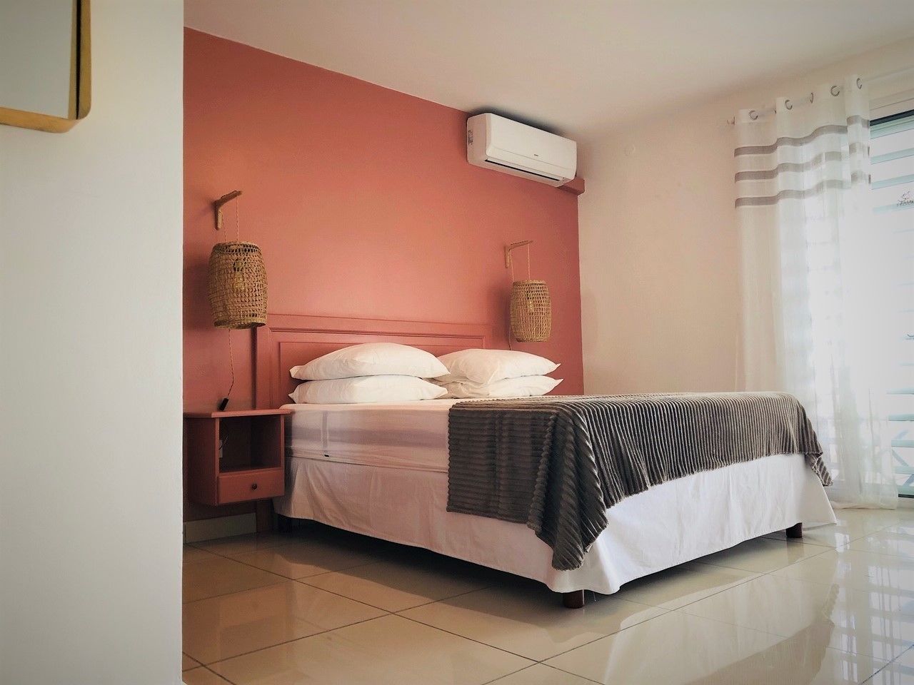 A bedroom with a bed, a nightstand, a wall-mounted air conditioner, and a window with curtains.