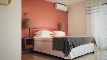 Un dormitorio con cama, mesita de noche, aire acondicionado instalado en la pared y ventana con cortinas.