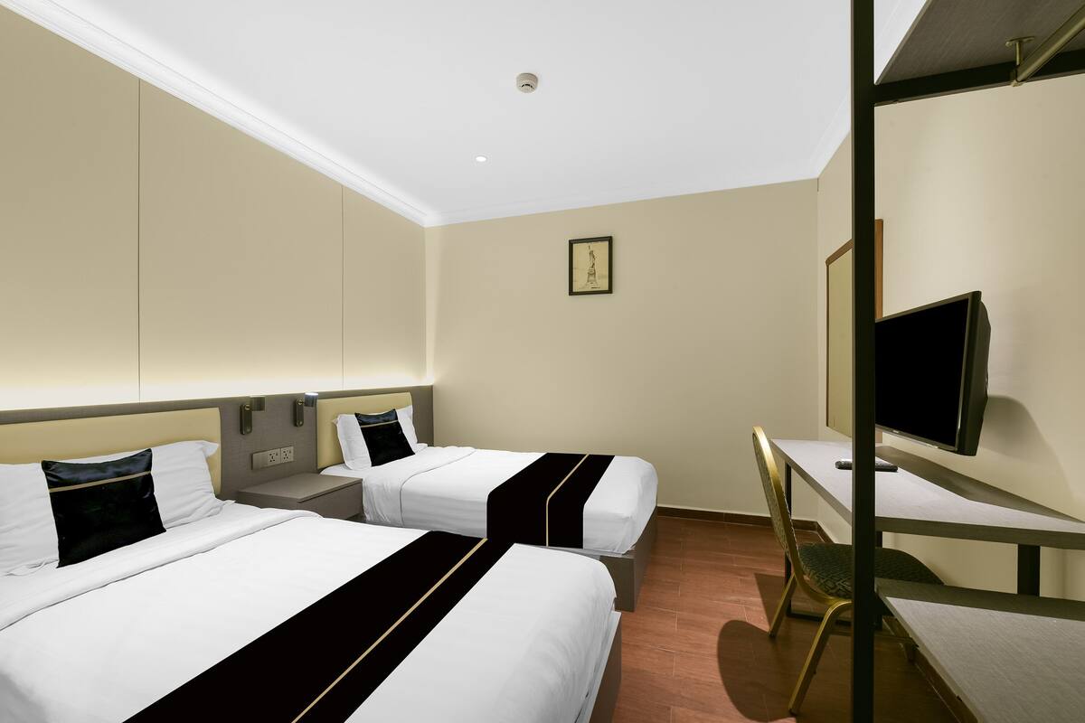Habitación de hotel con dos camas, un escritorio, una silla, un televisor y un cuadro en la pared.