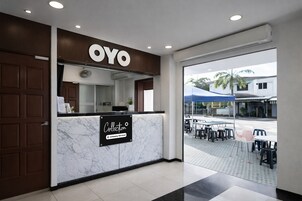 Zona de recepción de un hotel con mostrador de mármol, un letrero que dice 'OYO Collection Company-Serviced' y vista al área de estar al aire libre.