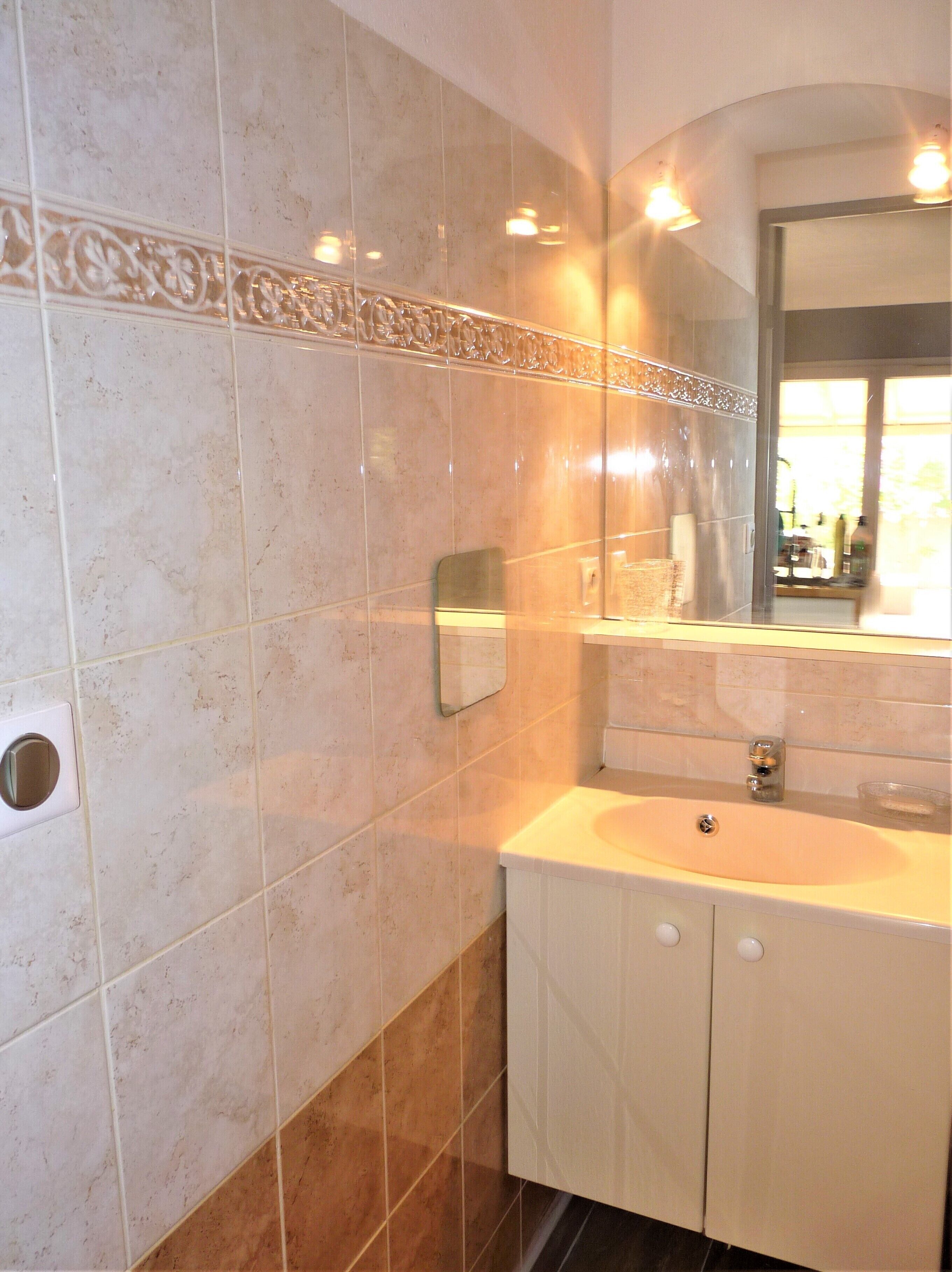 Un baño con lavamanos, espejo y dispensador de toallas en la pared.