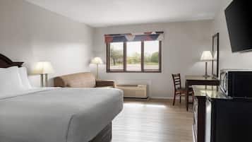 Una camera d'albergo con un letto, due lampade ai comodini, una scrivania con una sedia, una televisione e una finestra vista alberi.