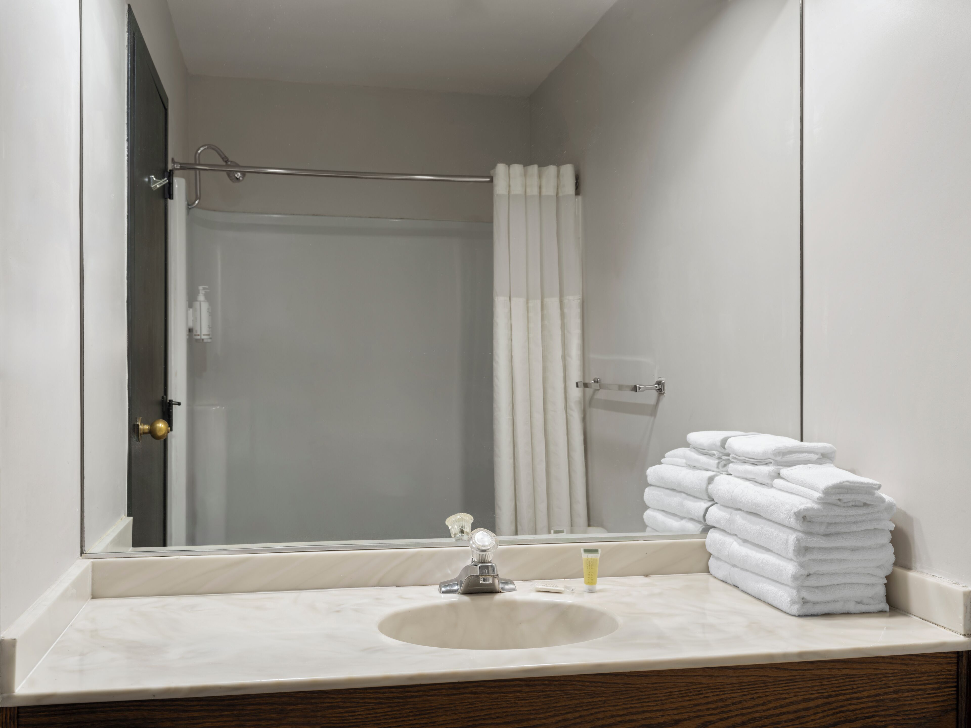 A bathroom with a sink, a mirror, a shower curtain, and a stack of towels.