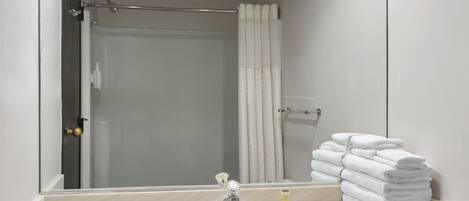 A bathroom with a sink, a mirror, a shower curtain, and a stack of towels.