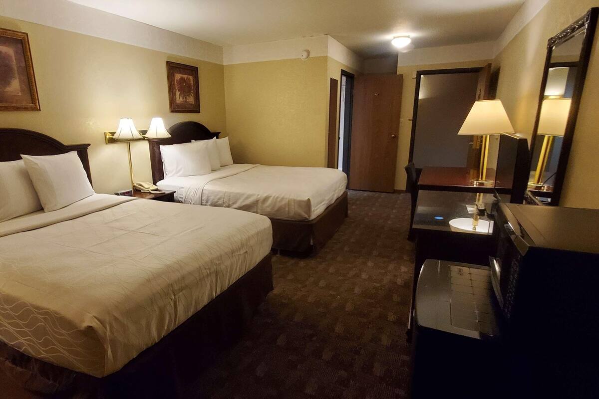 A hotel room with two beds, a desk with a lamp, a mirror, and a dresser.