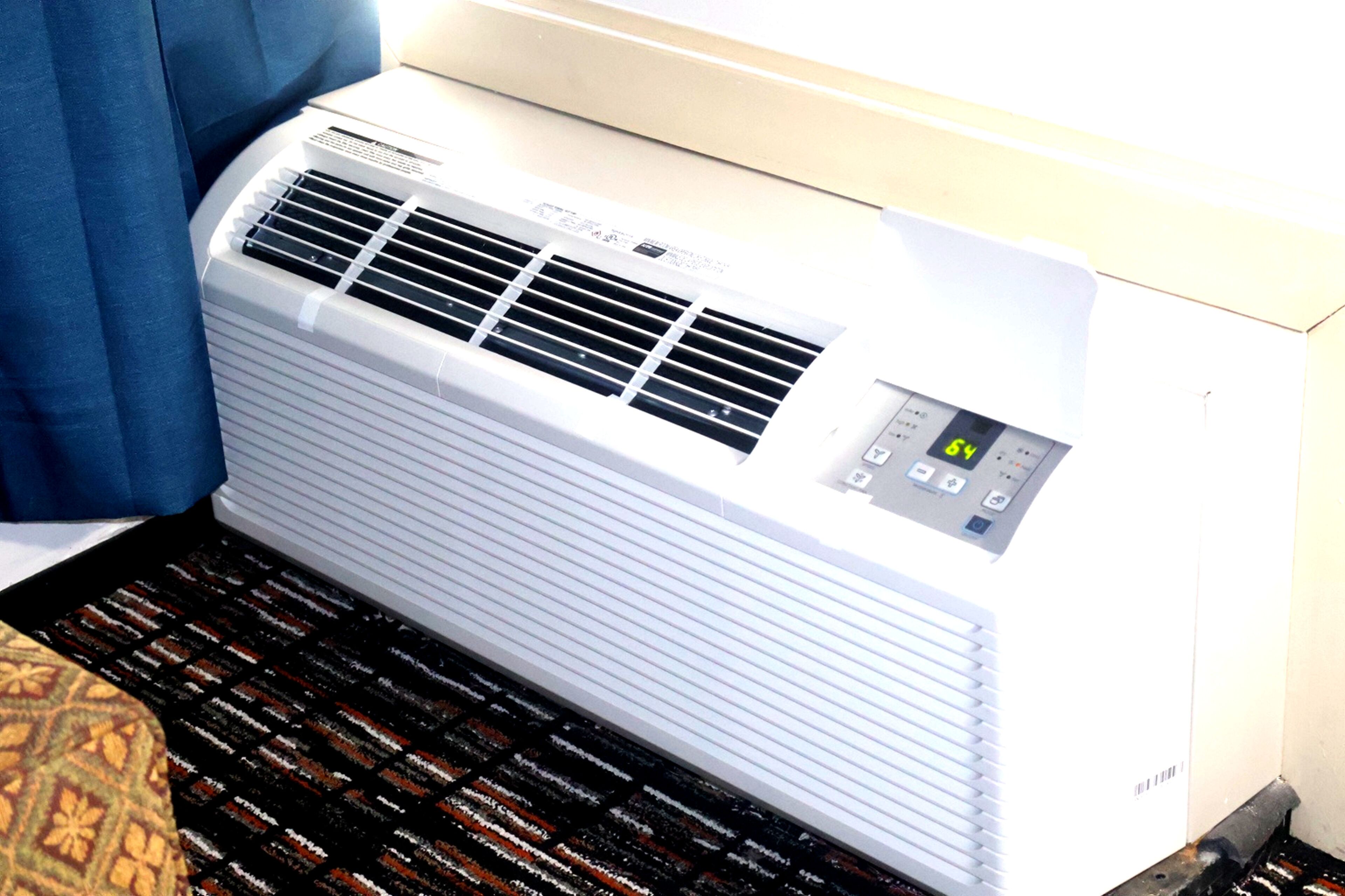 Eine weiße Klimaanlage mit Bedienfeld auf einem gemusterten Teppich.