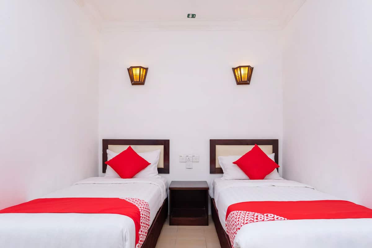 A hotel room with two beds, each with a red pillow and a white bedspread. There are two wall-mounted lights above each bed.