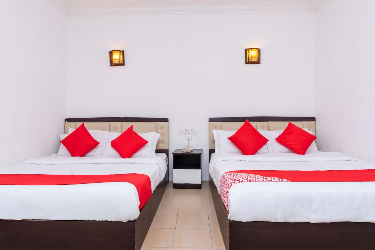A hotel room with two beds, each with a red and white bedspread, and two wall-mounted lights.