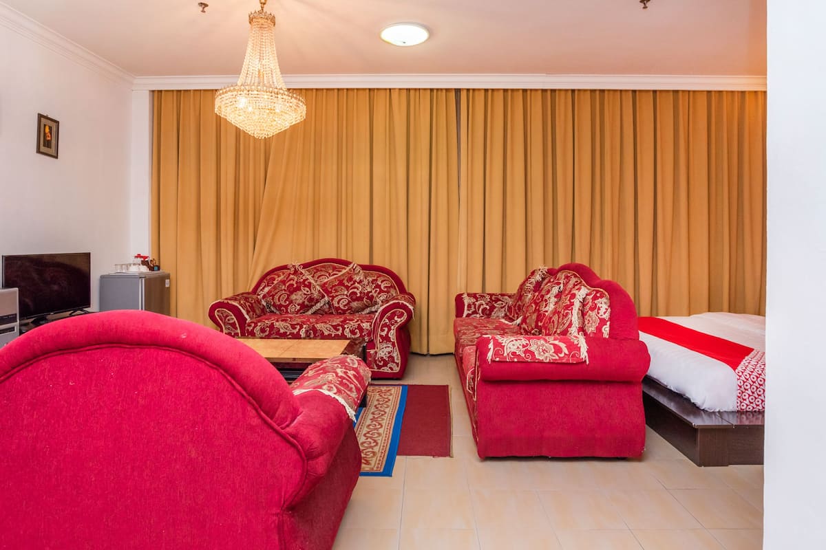 A hotel room with a large bed, two red sofas, a television, and a minibar.