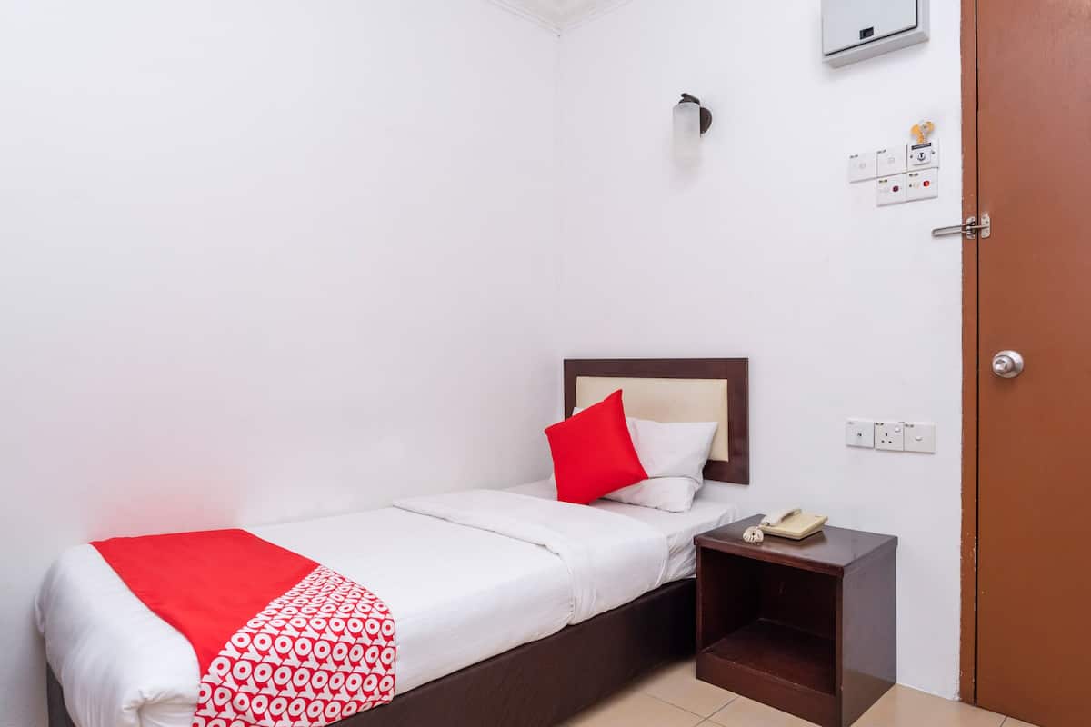 A single bed with a red and white patterned blanket, a wooden headboard, and a bedside table with a book and a phone.