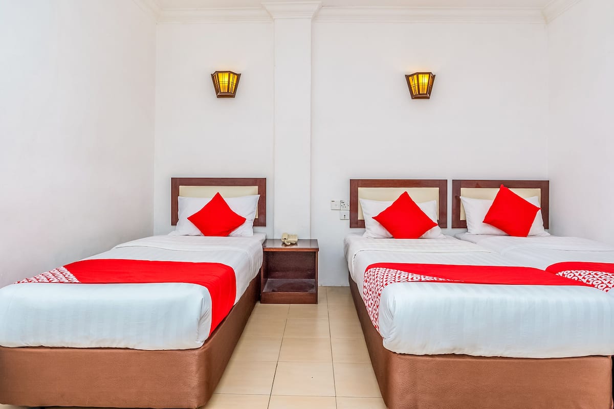 A hotel room with two beds, each with a red and white bedspread, and two wall-mounted lamps.