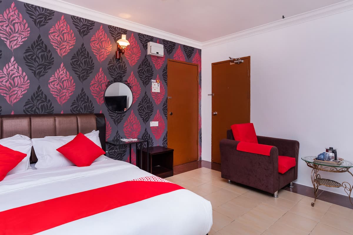 A hotel room with a large bed, a chair, a small table, and a mirror on the wall.