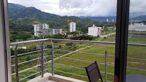 A balcony with a metal railing overlooking a green landscape with buildings and a construction crane. - mirador de los andes (Ibagué)