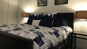 A neatly made bed with a patterned bedspread, two wall-mounted lamps, and two framed pictures on the wall.