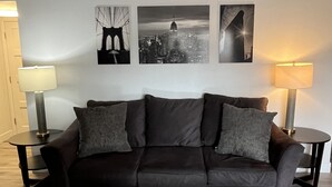 A modern living room with a dark brown leather sofa, two side tables with lamps, and three framed pictures on the wall.