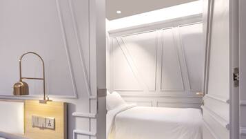 A modern bedroom with a bunk bed, a bedside table with a lamp, and a wall-mounted light switch.
