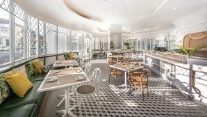 Un restaurante moderno con un patrón geométrico en el suelo, muebles blancos y grandes ventanales con vistas a la ciudad.