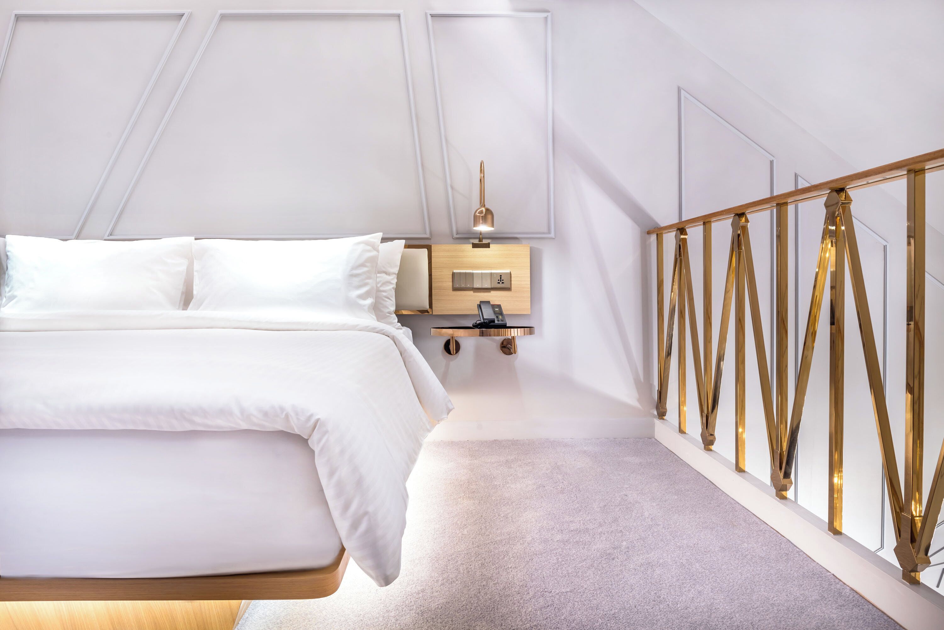 A modern bedroom with a large bed, a bedside table with a lamp, and a decorative railing.