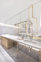 A modern bathroom with a white vanity, gold-framed mirror, and marble flooring.