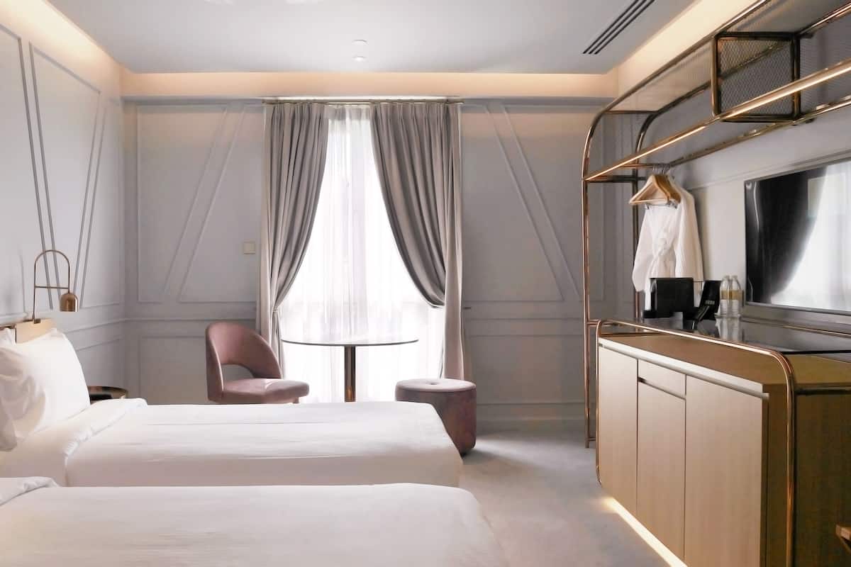 A hotel room with a bed, a chair, a TV, and a minibar.