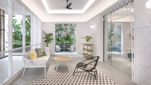 Un interior moderno con un sofá blanco, una mesa redonda y una silla de mimbre. Hay plantas en macetas y una partición de vidrio.