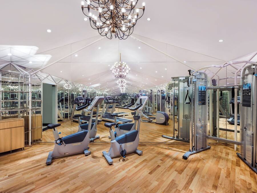 A gym with exercise equipment, wooden flooring, and a large chandelier.