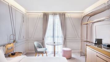Una habitación de hotel con cama, una mesa redonda, una silla, un pequeño otoman y un armario.