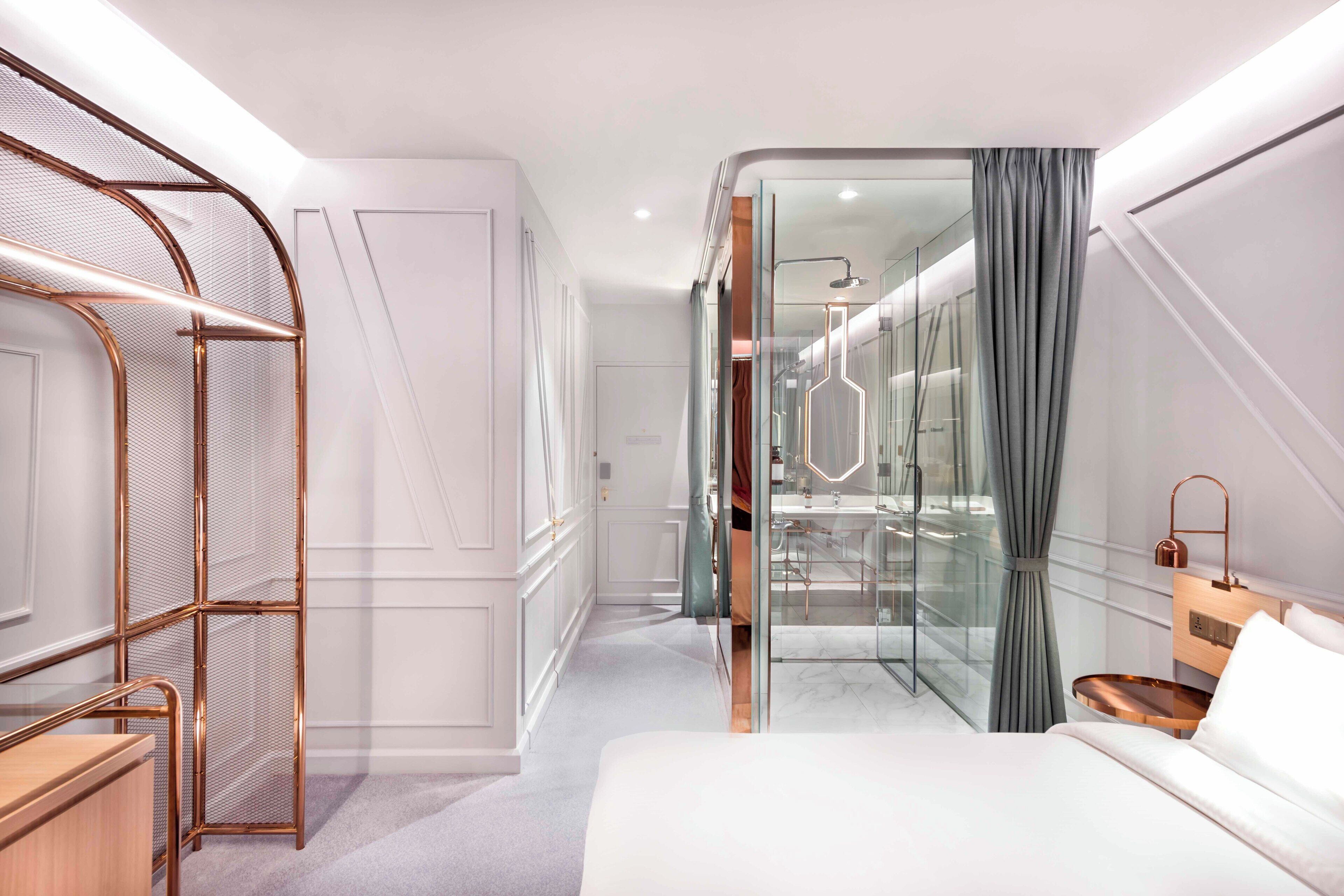 A modern hotel room with a walk-in closet, a glass shower enclosure, and a bed with a wooden side table.