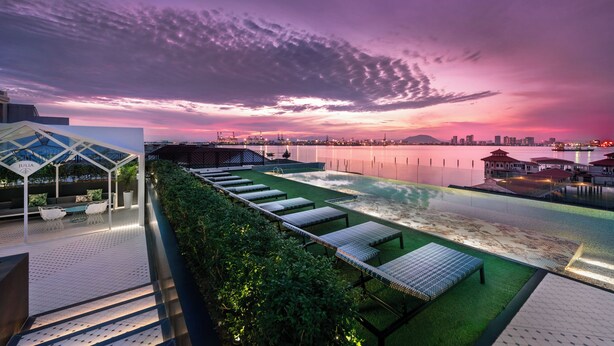 Una terraza en la azotea con vistas a un horizonte urbano al atardecer, piscina y zonas de estar al aire libre.