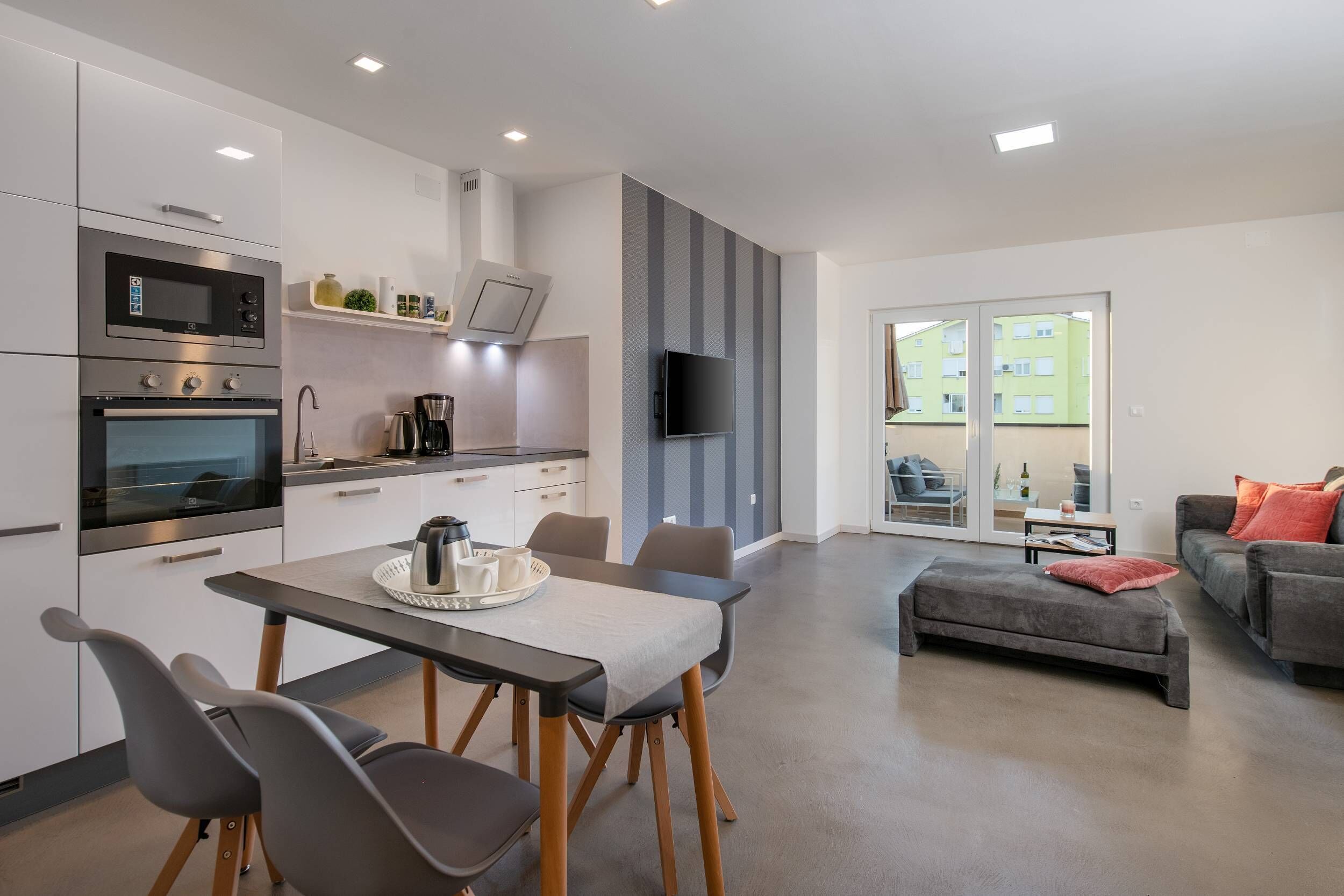 A modern kitchen with built-in appliances, a dining area with a table and chairs, and a living space with a sofa and a TV.