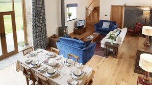 A spacious living room with a blue sofa, a dining table set for four, and a staircase leading to another level.