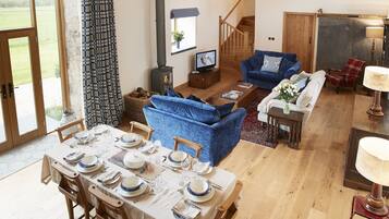 A spacious living room with a blue sofa, a dining table set for four, and a staircase leading to another level.