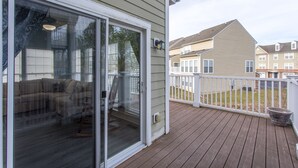 A residential deck with a sliding glass door leading to a living area with a sofa and a chair. - Perfect family vacation, Open floor plan, Relaxed coastal living (Millville)