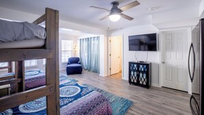A room with bunk beds, a ceiling fan, a TV, and a door leading to another room. - Perfect family vacation, Open floor plan, Relaxed coastal living (Millville)