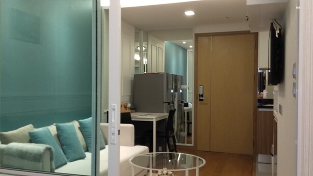 A modern living room with a glass partition, a white sofa, a glass coffee table, and a kitchen area in the background. - Resort Style Condo @Heart of Bangkok- Quiet location- Fast Wifi -24 Hour Checkin (Bangkok)