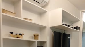 A modern room with white walls, a built-in TV, and a round white table with a vase of flowers. Shelves are stocked with various items, including a framed picture and a small wooden box. - Resort Style Condo @Heart of Bangkok- Quiet location- Fast Wifi -24 Hour Checkin (Bangkok)