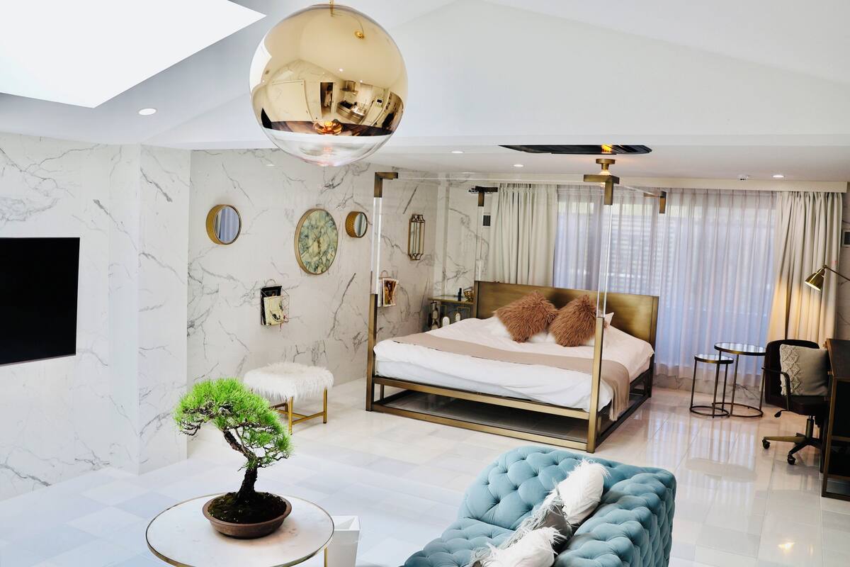 Une chambre moderne avec un grand lit, un miroir rond, un luminaire au plafond et une petite table sur laquelle est posée une plante.