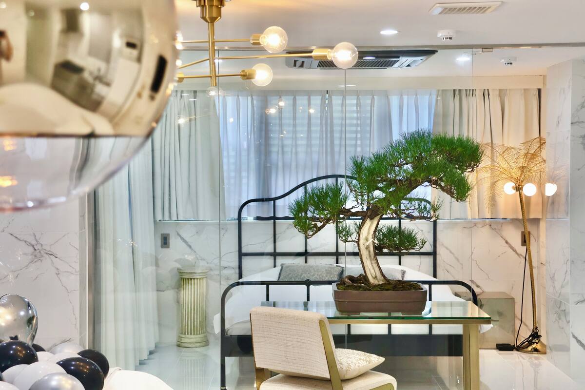 Une chambre d’hôtel moderne avec une table à manger en verre, un bonsaï en pot et un lustre.