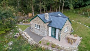 Une maison en pierre avec un toit végétalisé, une cheminée et une terrasse aménagée avec du mobilier d’extérieur.